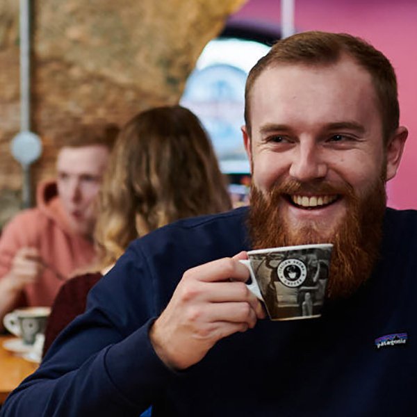 Man drinking a coffee with a couple in the background